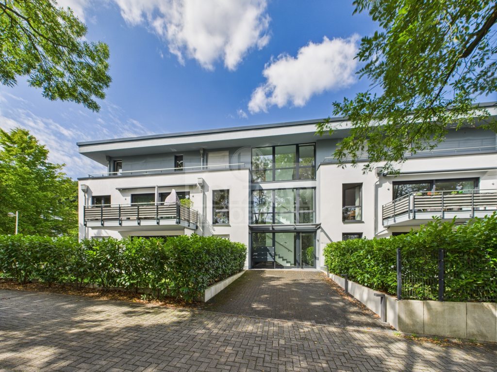 Zeitgemäßes Wohngebäude mit Glasfront im Eingangsbereich und mehreren Balkonen, umgeben von Grünflächen